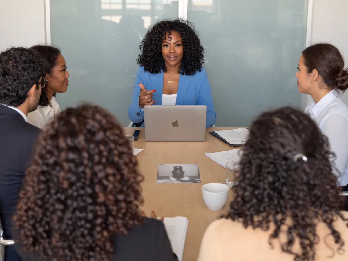 Zuleema Isaac at the head of a conference table, walking a client team through a new dashboard on a laptop